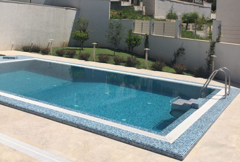 Betonpool 6×3,5 m mit einer Kombination aus Glasmosaik und rutschfester Fliese.